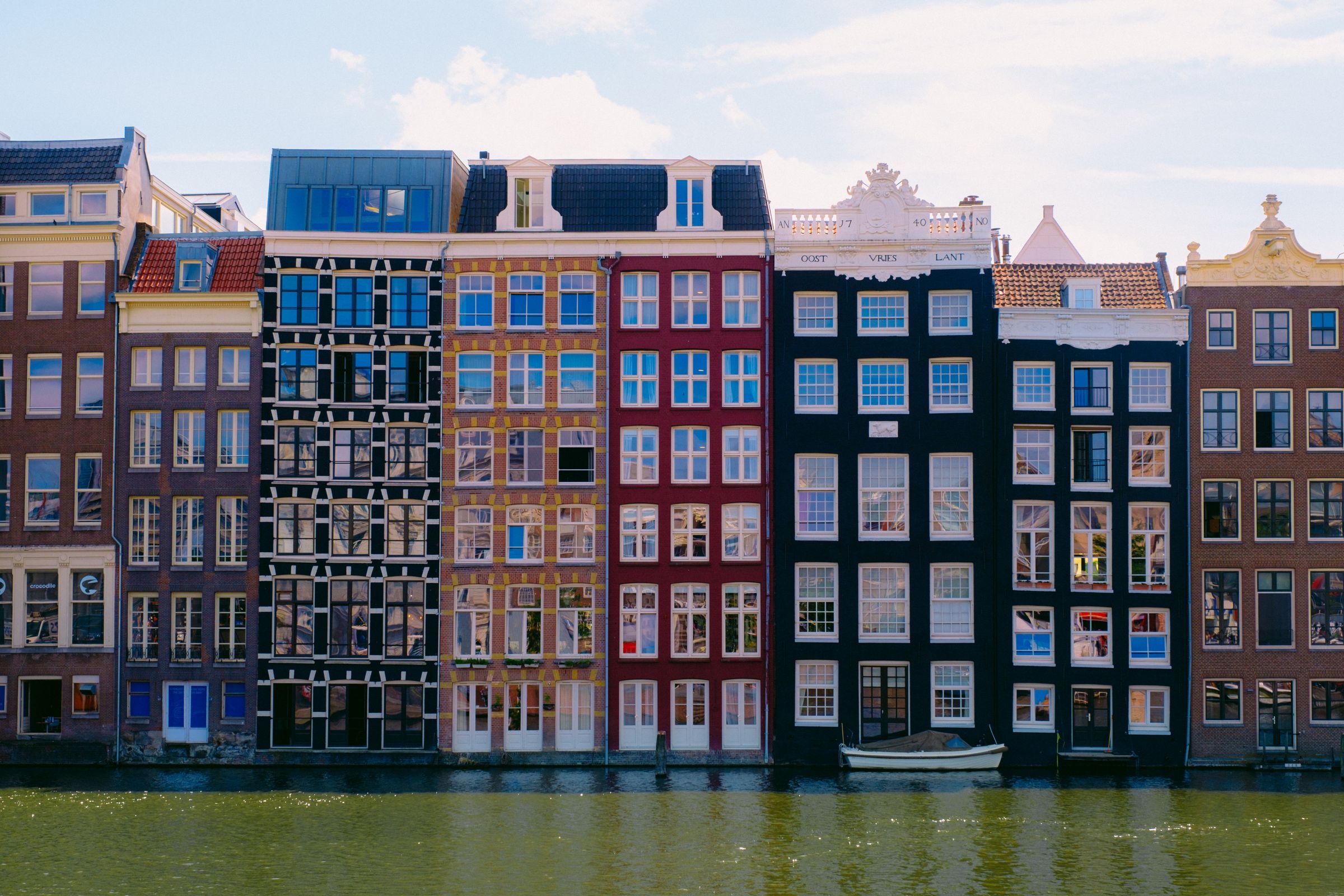 Brick canal houses used as offices along an Amsterdam canal on a sunny day.