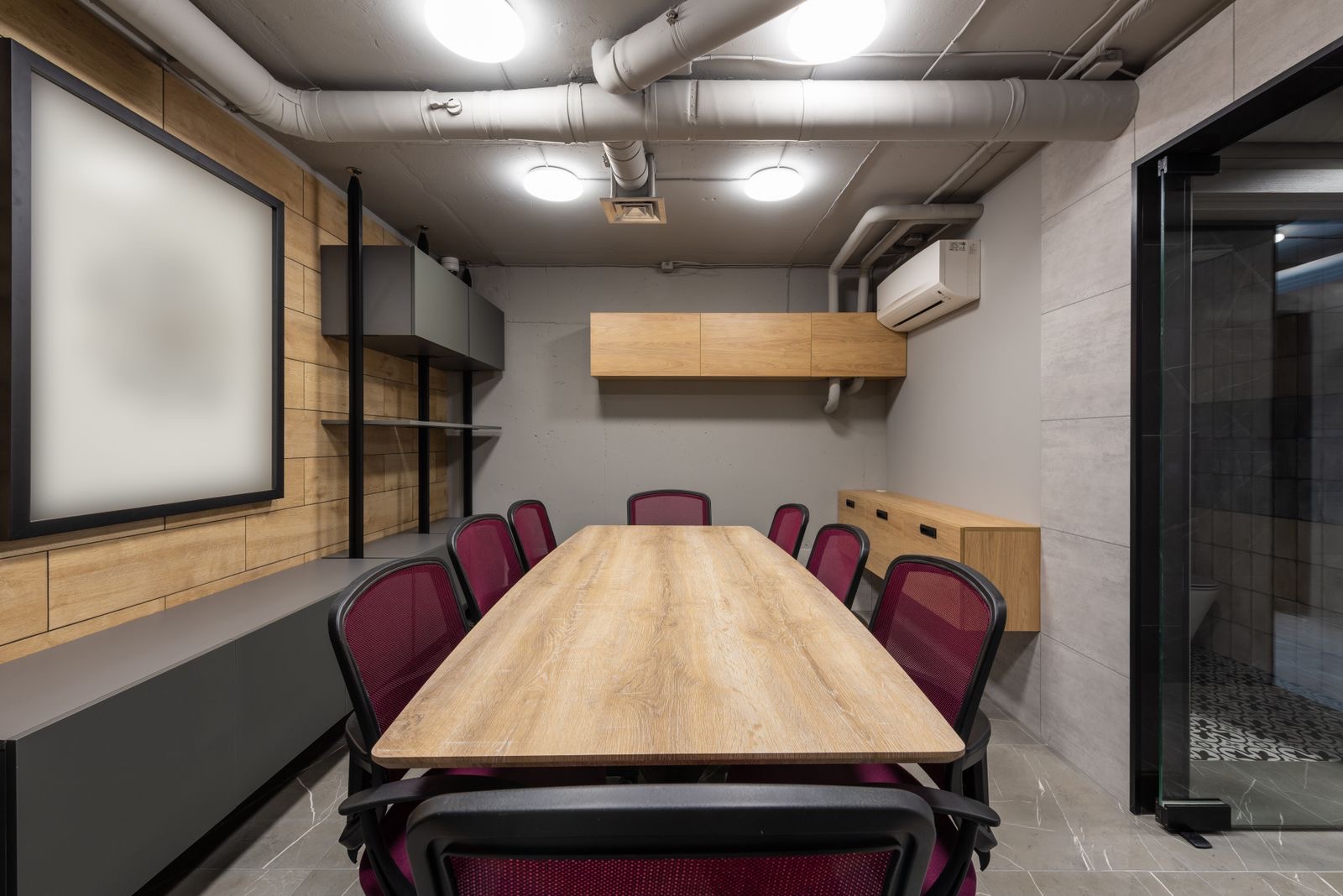 A small meeting room with a wooden table and chairs lit by a tall window.